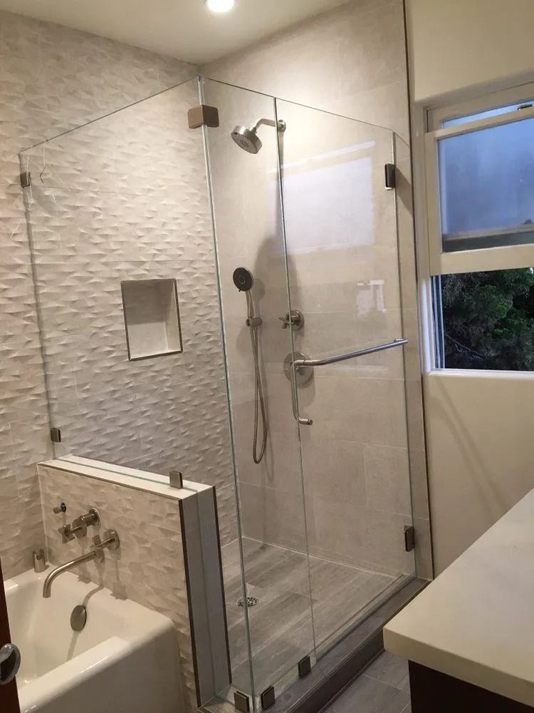 Bright modern bathroom with glass shower enclosure, tiled walls, sink, and window.