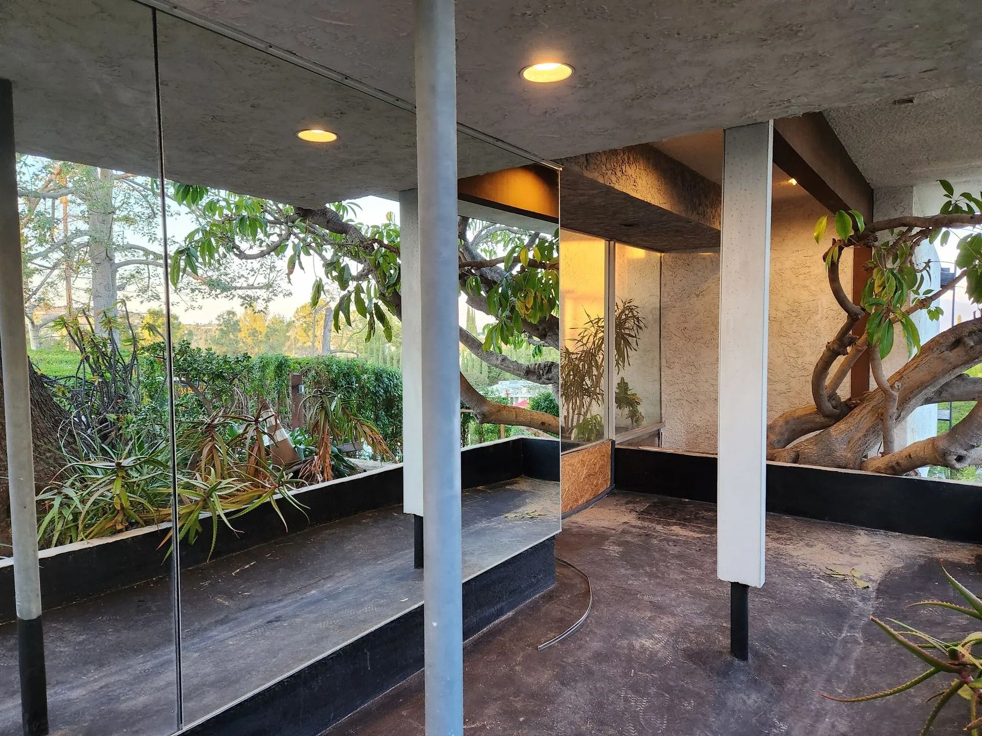Covered patio with concrete pillars, built-in benches, and garden view at dusk