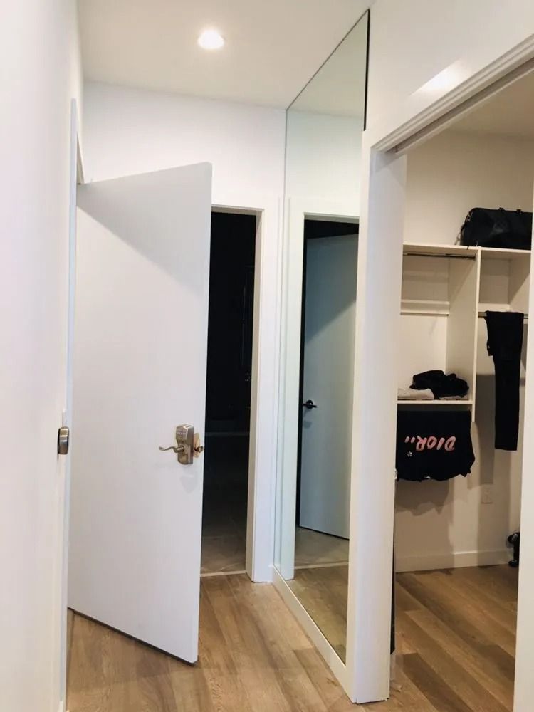 Open white bedroom closet with mirrored door, wooden floor, and an open doorway to a hall