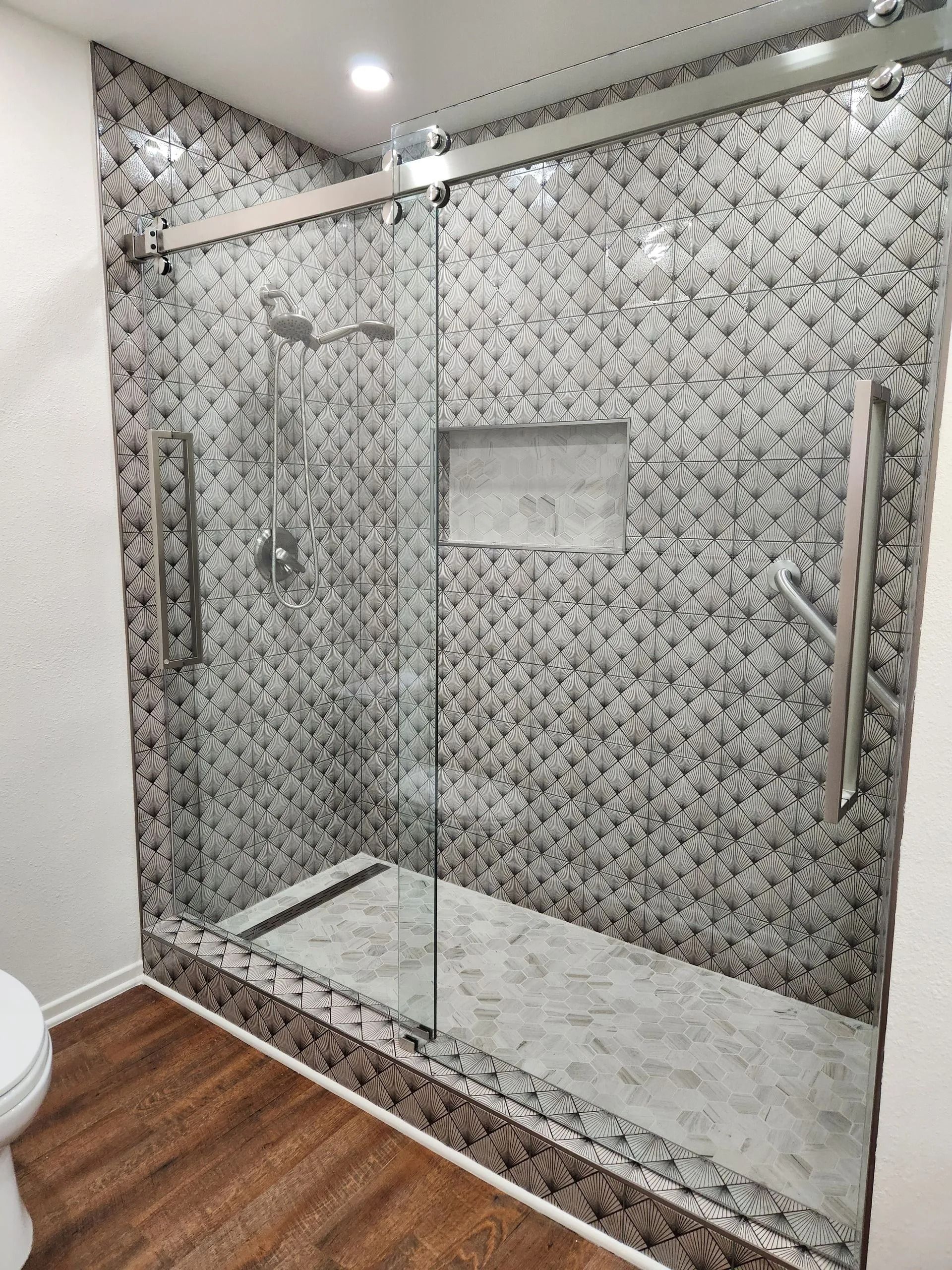 Modern bathroom with a glass walk-in shower, marble-pattern walls, and wood-look flooring.