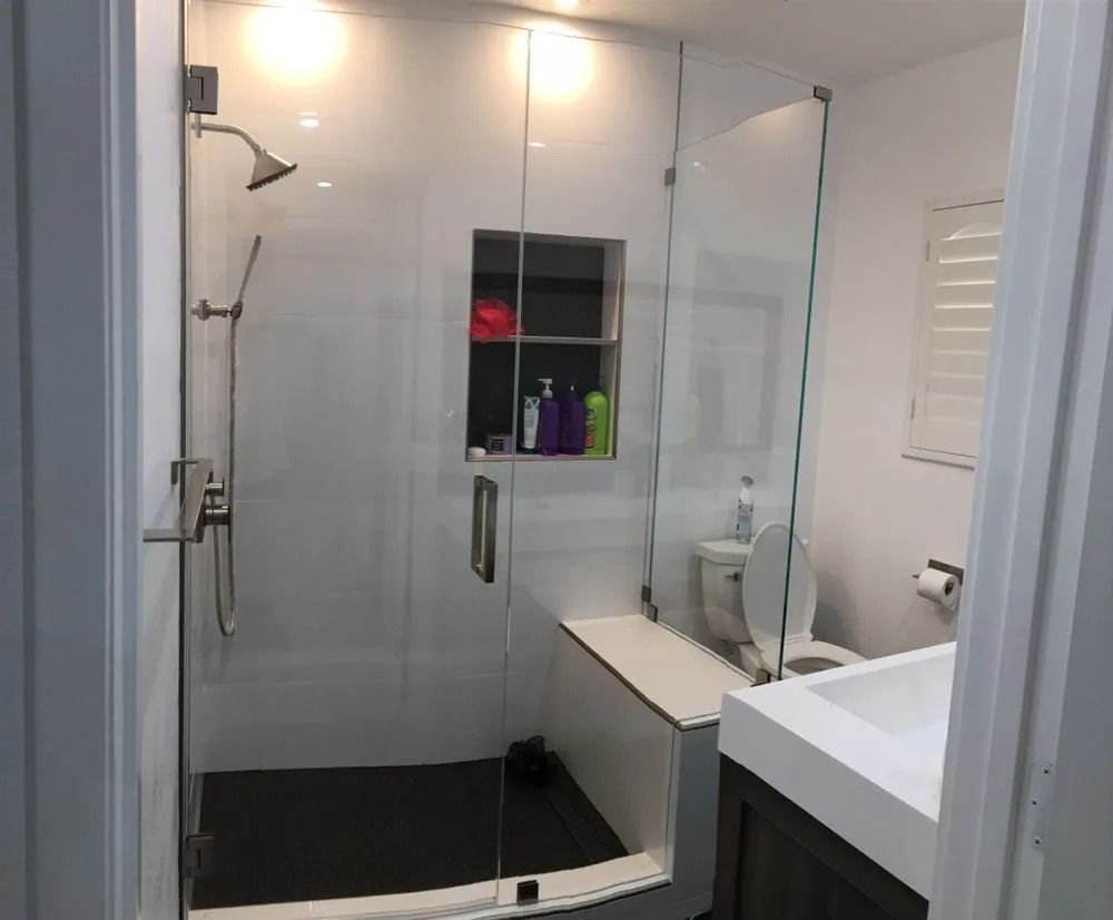 Modern bathroom with glass shower, white tile, black floor, and built-in shelf with toiletries