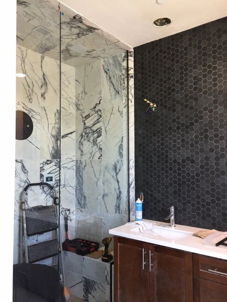 Modern bathroom with marble shower, dark tiled wall, and vanity sink.