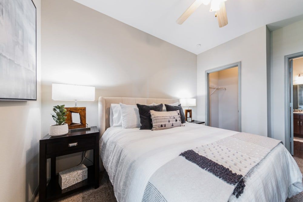 a bedroom with a bed, nightstand, lamps, and a ceiling fan at Marquis at Katy in Katy, TX.