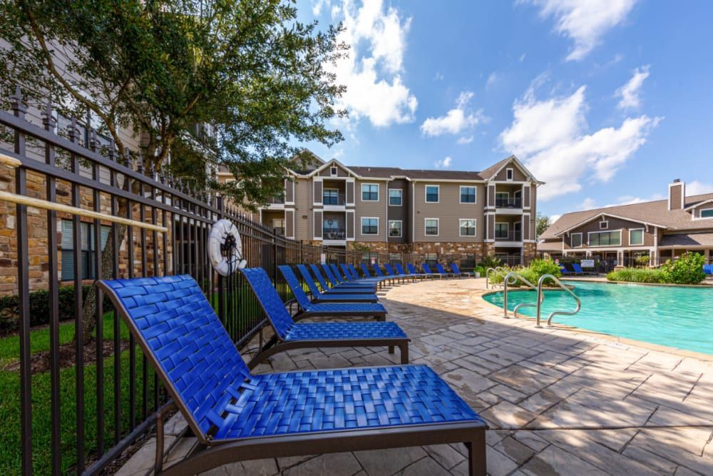 a row of blue lounge chairs sitting next to a swimming pool in front of a building at Marquis at Katy in Katy, TX.