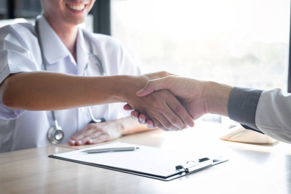 Un medico stringe la mano a un paziente seduto alla scrivania.