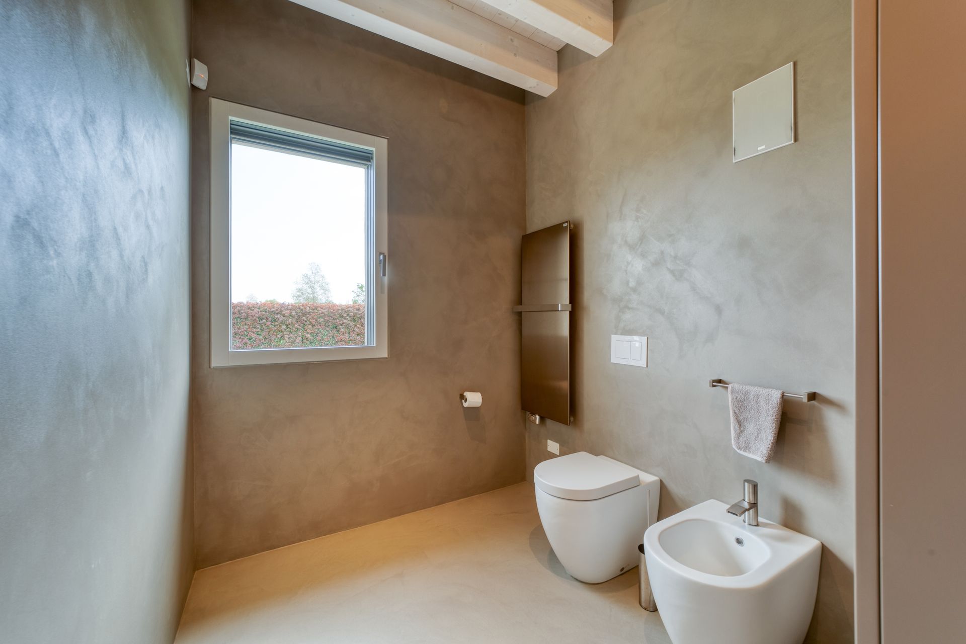 Bagno moderno con finestra, WC e bidet bianchi, pareti e pavimento beige.