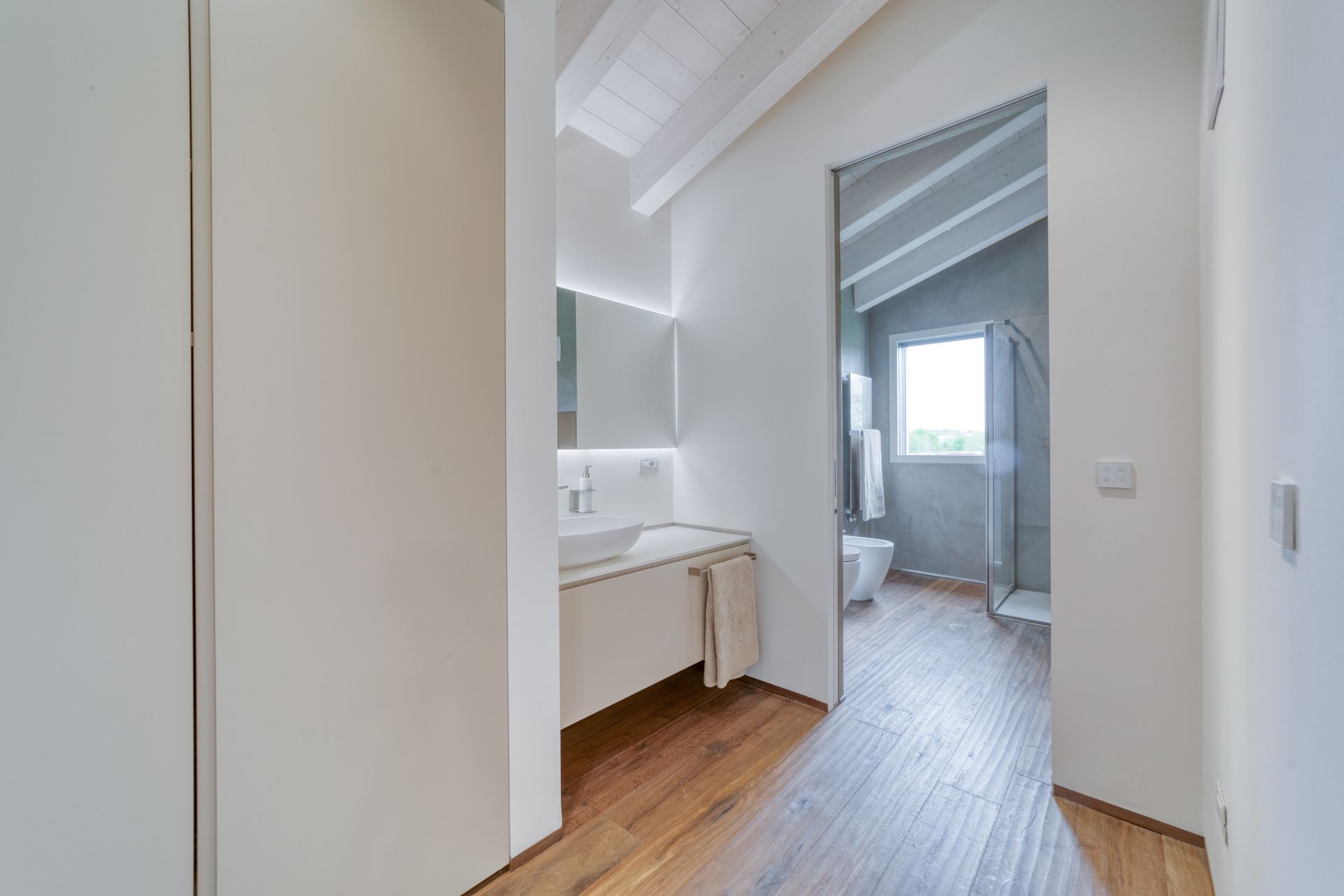 Luminoso corridoio con mobiletto bianco, pavimento in legno e porta che conduce a una camera da letto con finestra.