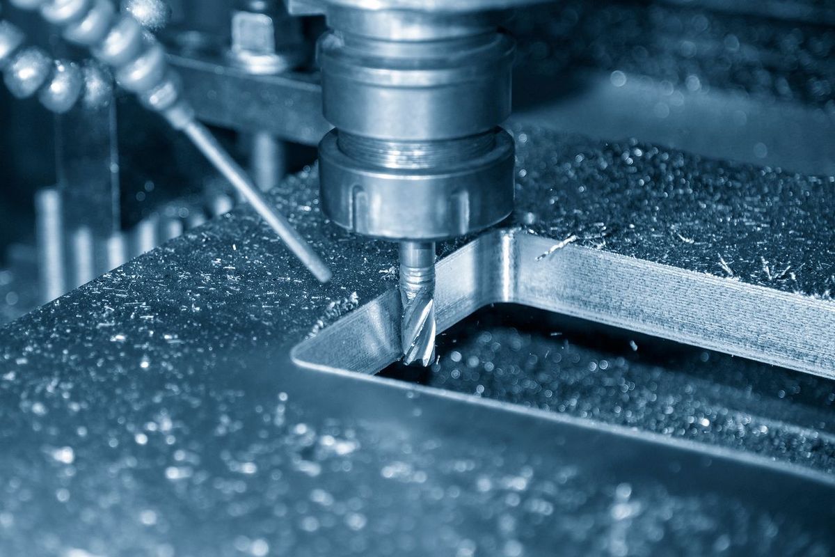 CNC milling machine cutting a metal part with a bit, generating shavings.