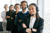 Outwork U.S customer service team with headsets, smiling, standing by a window, arms crossed.