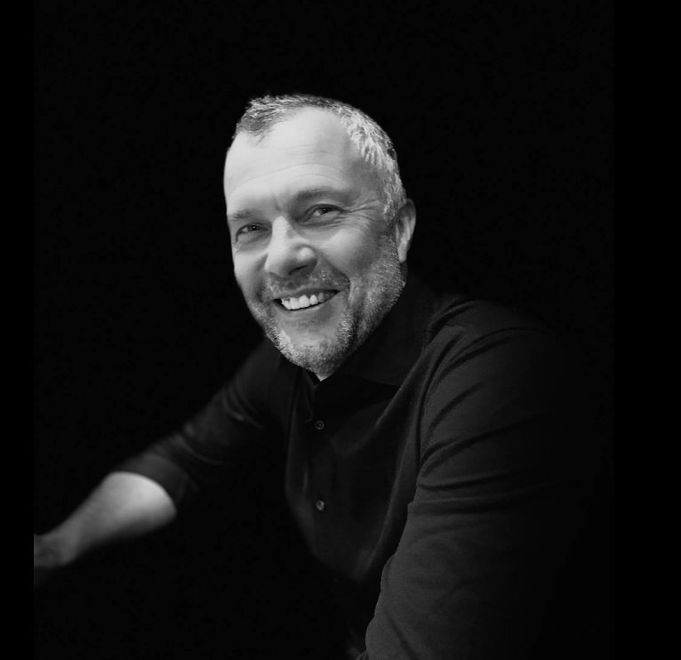 A man with a beard is smiling in a black and white photo.