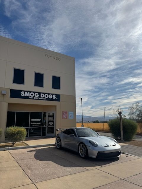 Silver sports car parked outside a Smoke Dogs storefront on a sunny day.