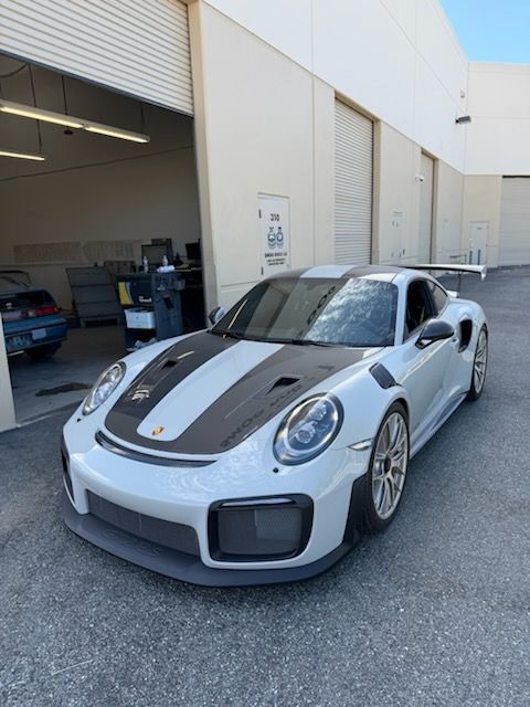 White sports car with black racing stripes parked outside a garage bay