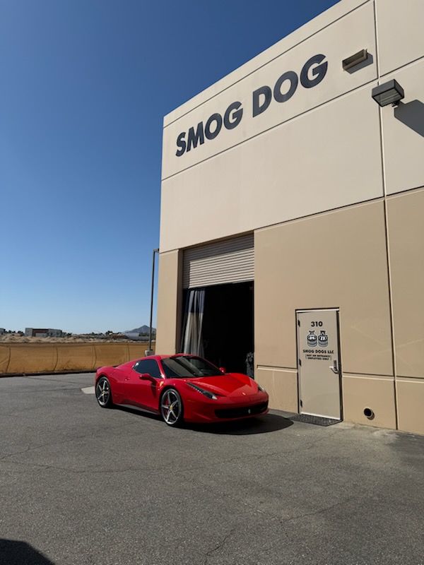 Red sports car parked outside a beige building labeled “SMOG DOG” on a sunny day
