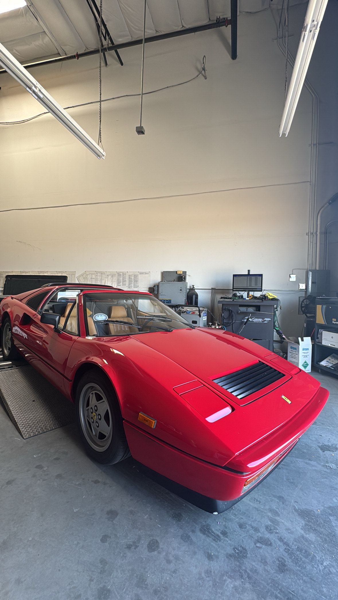 Red sports car in a garage/workshop with tools and equipment in the background