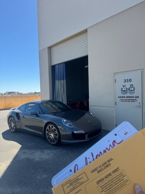 Gray sports car parked outside a white industrial building with an open garage door and a sign reading 310