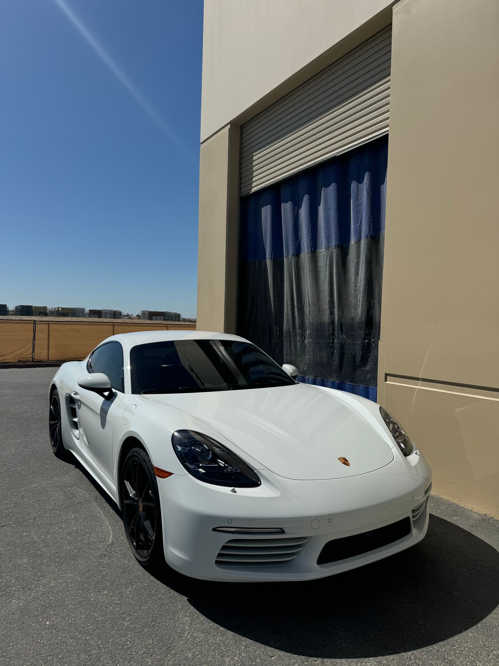 White sports car parked by a beige building with blue curtains in bright sunlight