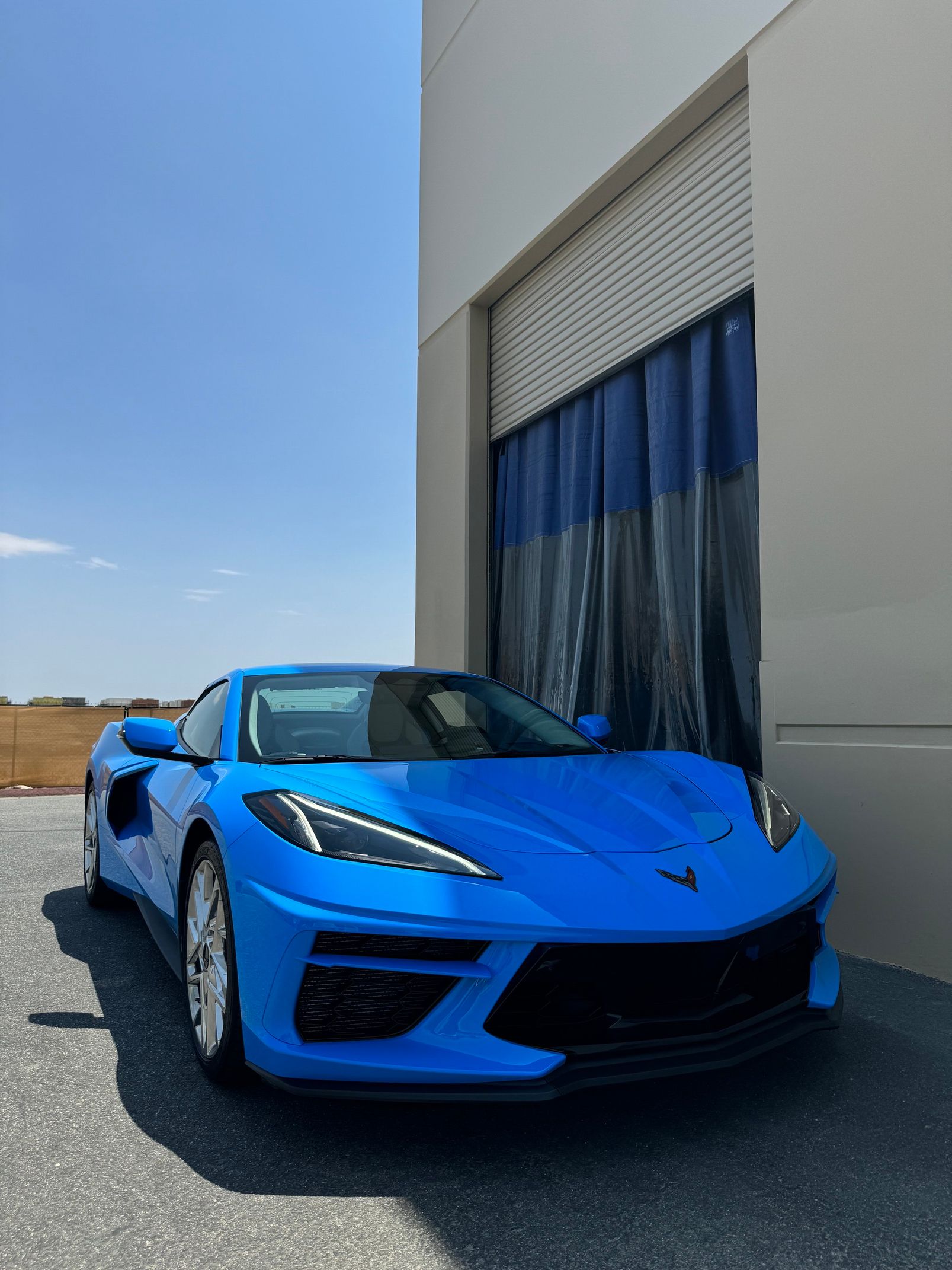 Blue sports car parked beside a building with curtains, on a sunny day