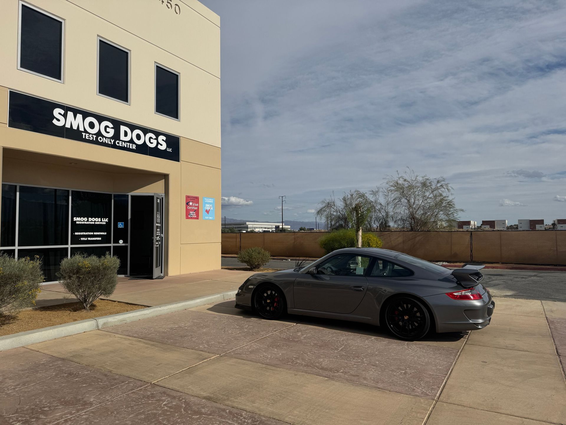 Gray sedan parked outside the Smog Dogs storefront on a sunny day.