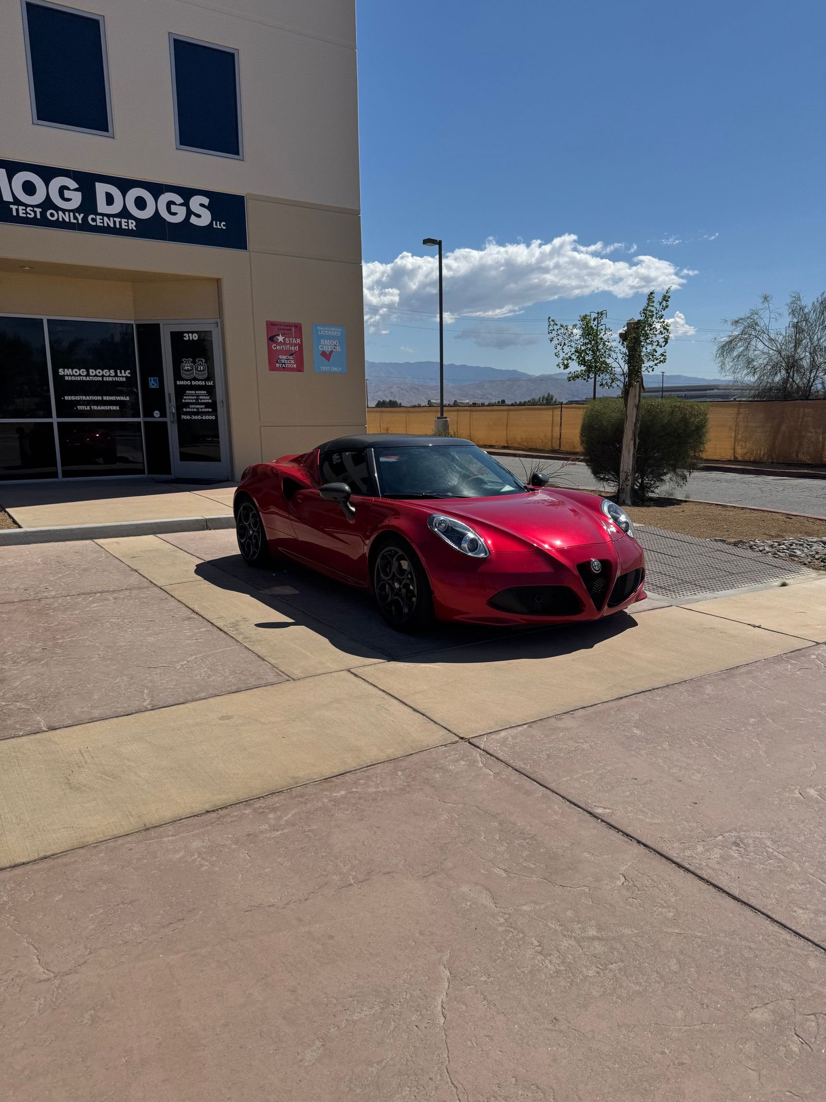 Red sports car parked outside a building with a “Hot Dogs” sign, under a bright blue sky.