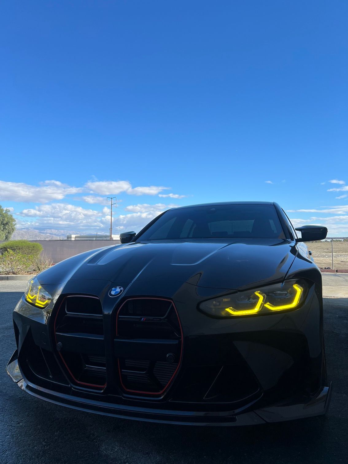 Black BMW coupe with yellow headlights parked outdoors under a blue sky.