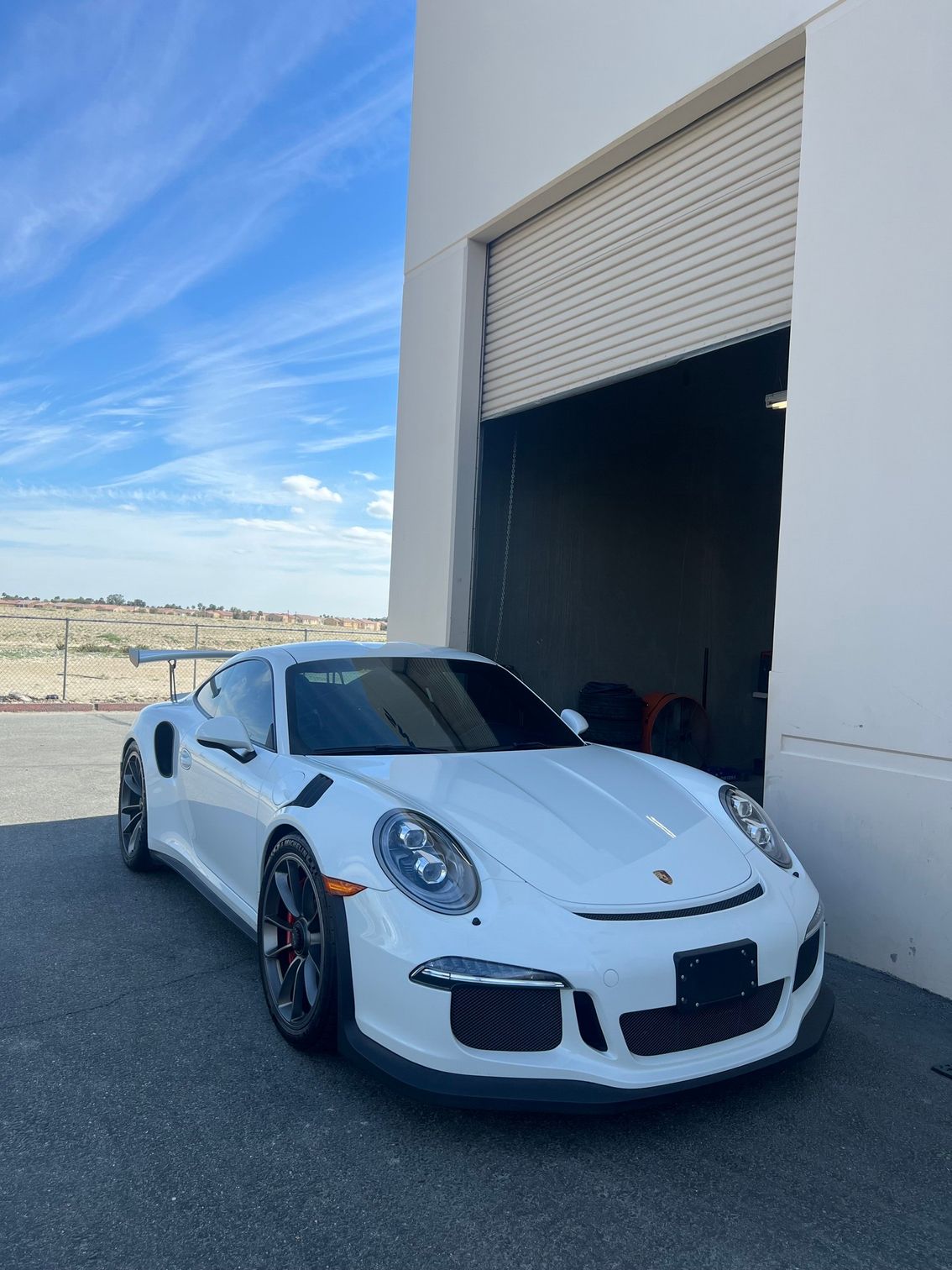 White sports car parked outside an industrial garage under a blue sky