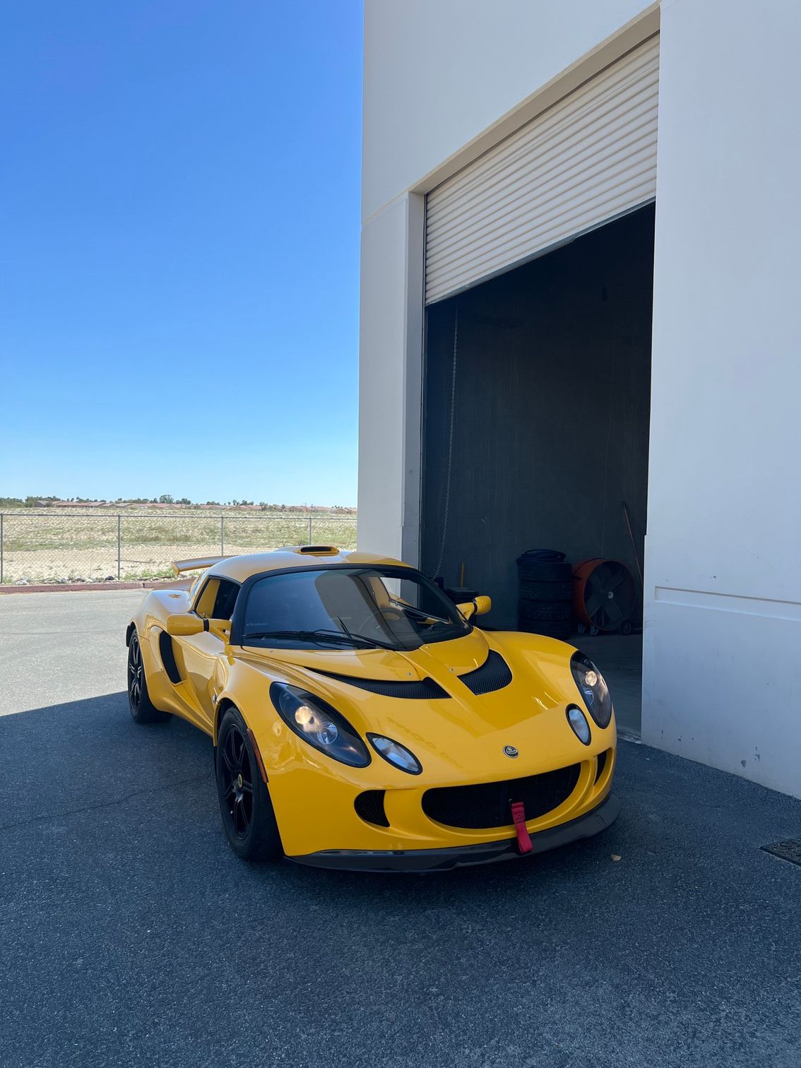 Yellow sports car parked outside a warehouse with an open garage door on a sunny day