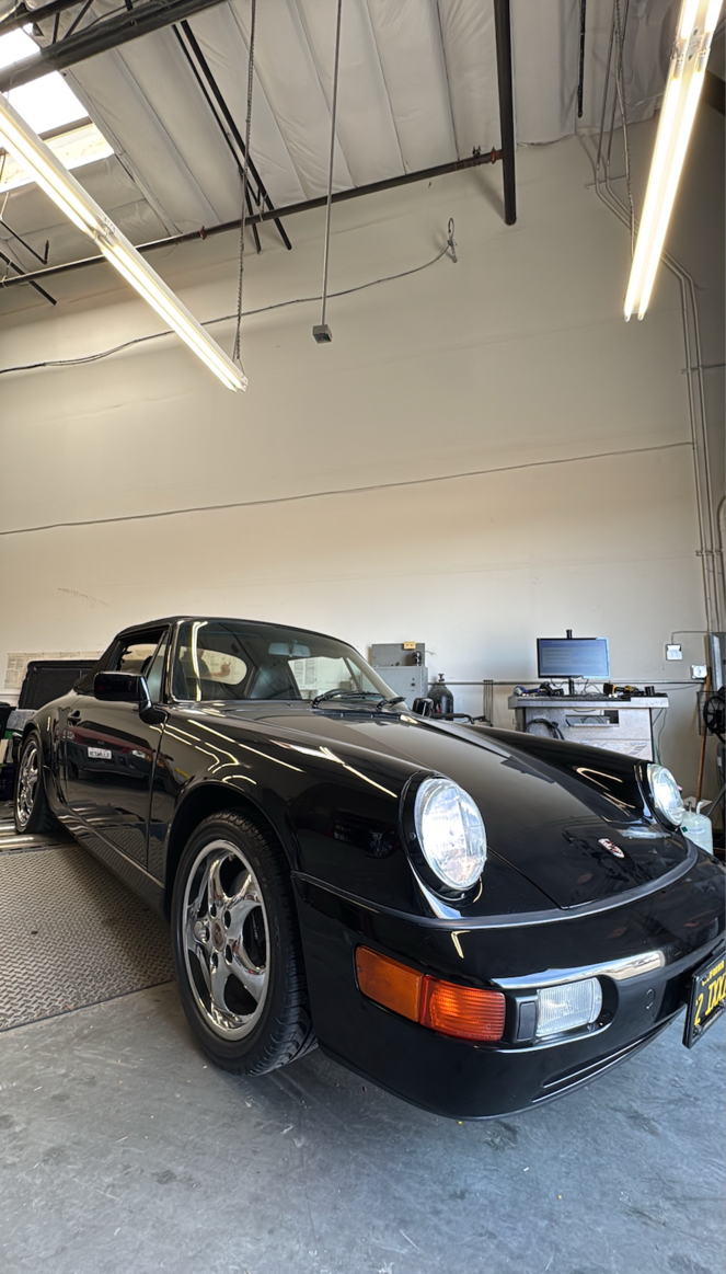 Black Porsche 911 parked in a garage with overhead fluorescent lights