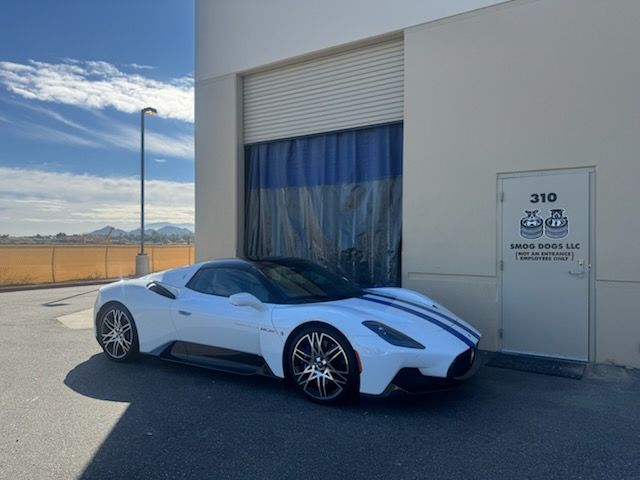 White sports car parked beside a warehouse door in an industrial lot under a blue sky