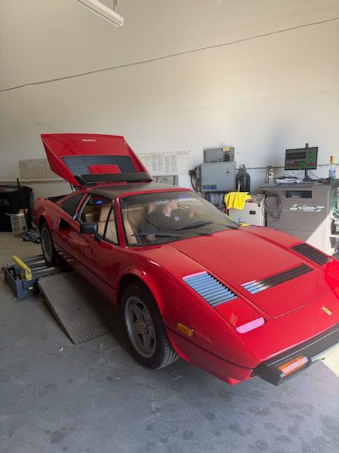 Red sports car in a garage with its hood open, showing the engine bay.