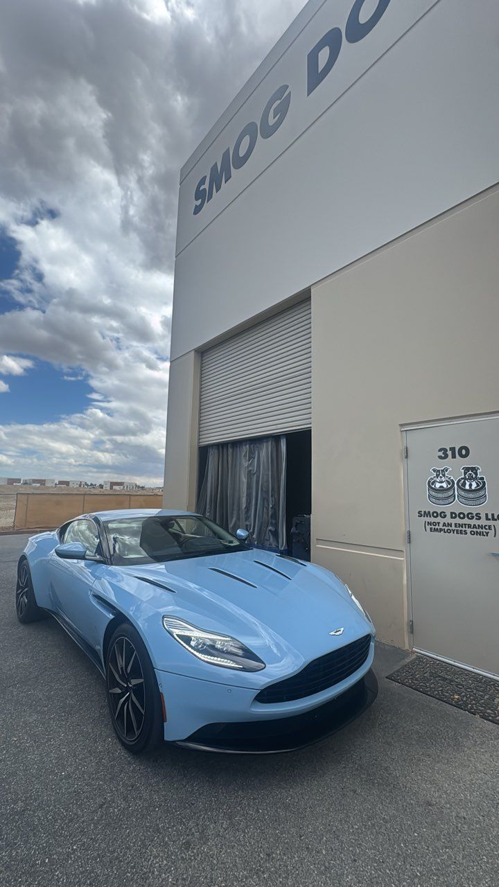 Blue convertible sports car parked outside a building with a roll-up door and cloudy sky overhead