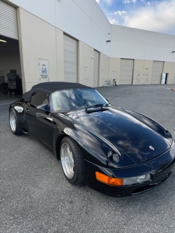 Black Porsche 911 parked outside a warehouse, front-left view on a paved lot
