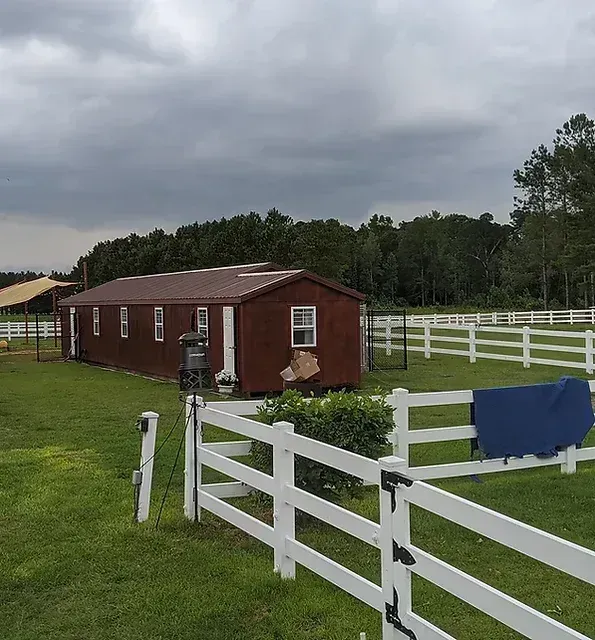 Red barn with white fences on a grassy field under a cloudy sky.
