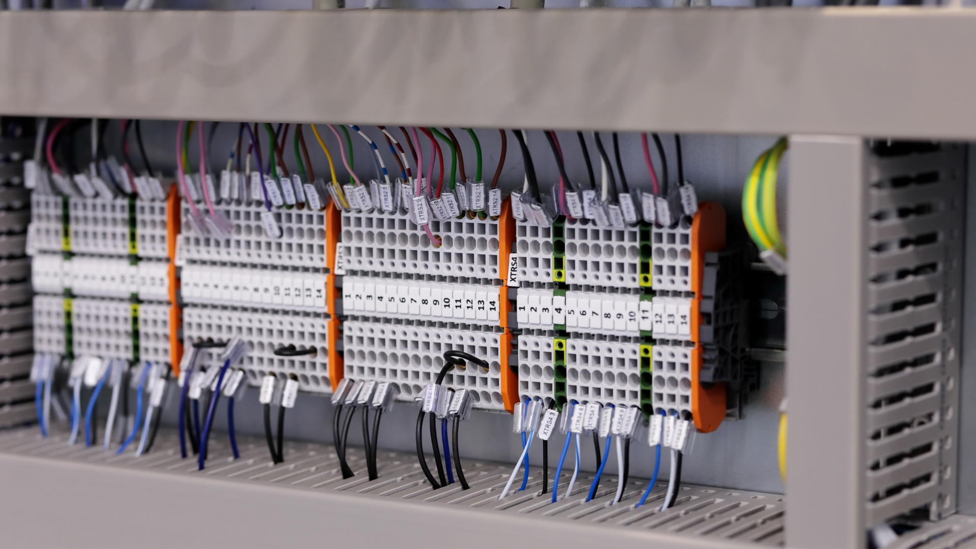 A gray industrial electrical cabinet features rows of labeled terminal blocks with connected multicolored wires.