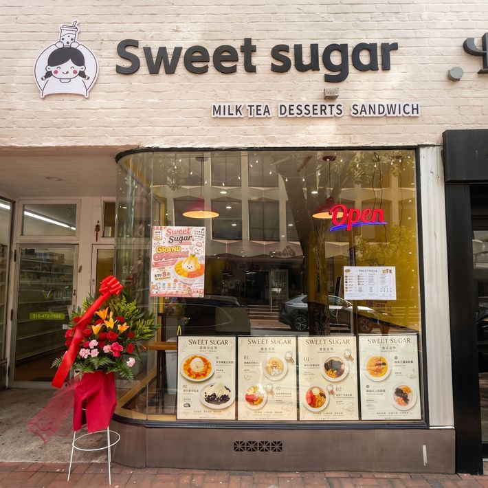 Sweet Sugar dessert shop storefront with glowing “Open” sign and flower stand outside