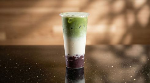 Layered green, white, and dark purple iced drink in a clear plastic cup on a dark table.