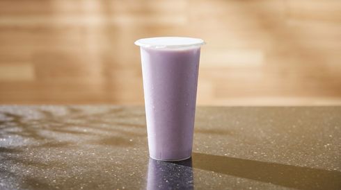 A tall lavender drink cup with a white lid stands on a reflective tabletop.
