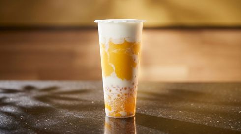 Clear plastic cup with layered yellow-orange drink on a dark tabletop, softly lit background