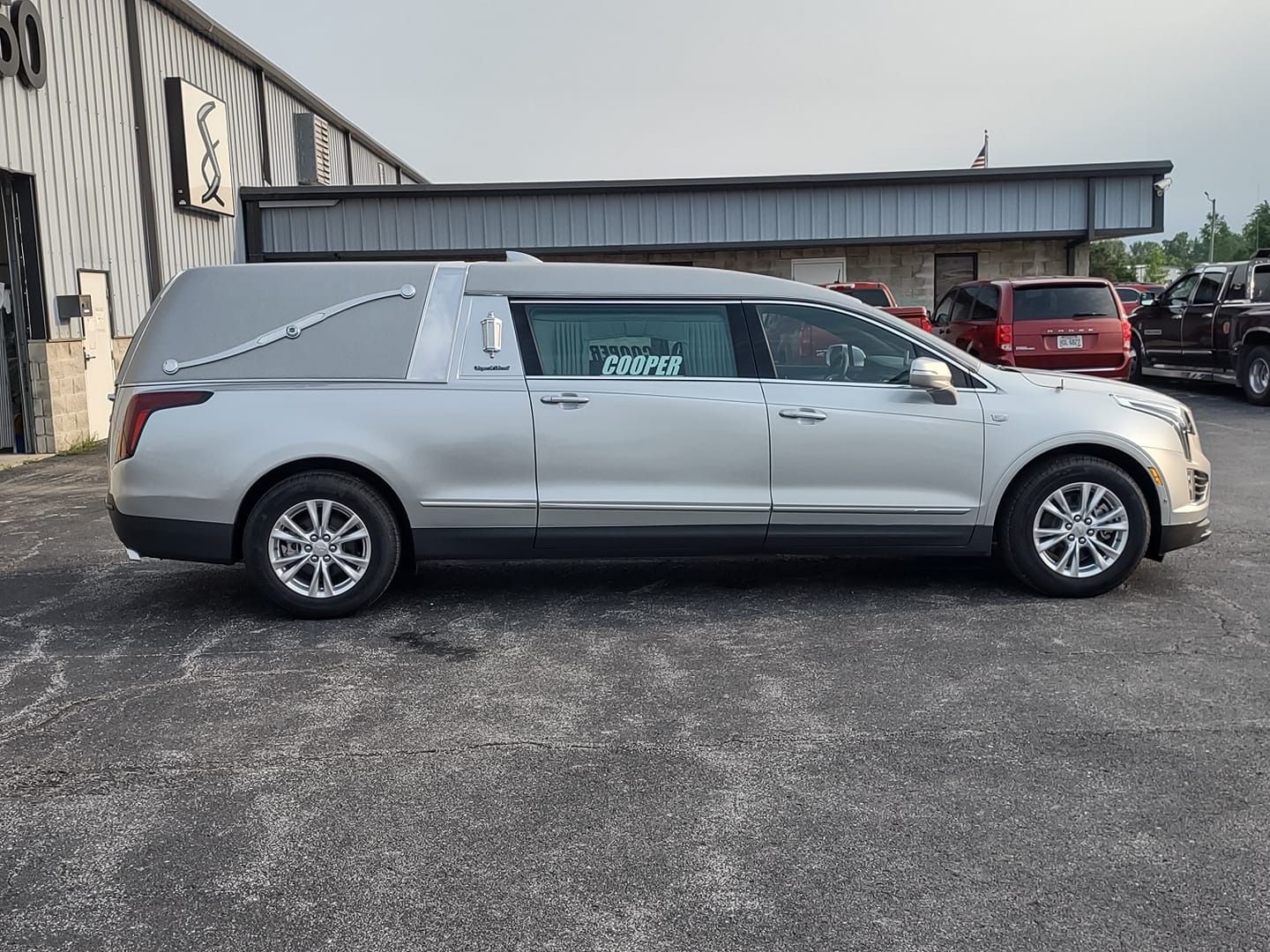 Silver hearse parked in a lot beside an industrial building, side view