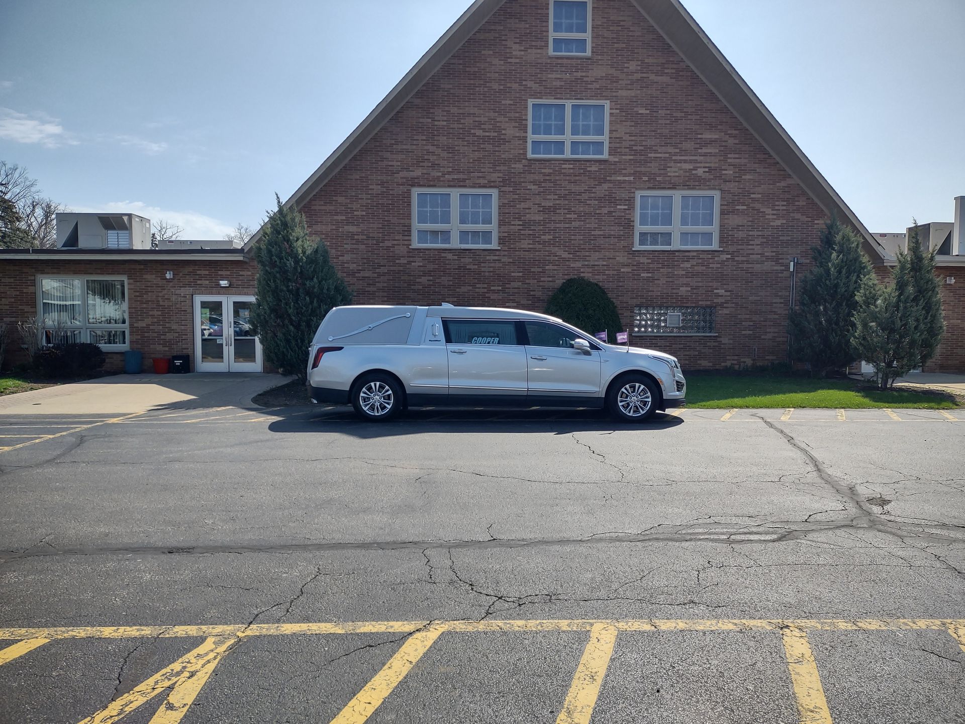 White SUV parked in front of a brick building with a steep roof and yellow parking lines in the foreground