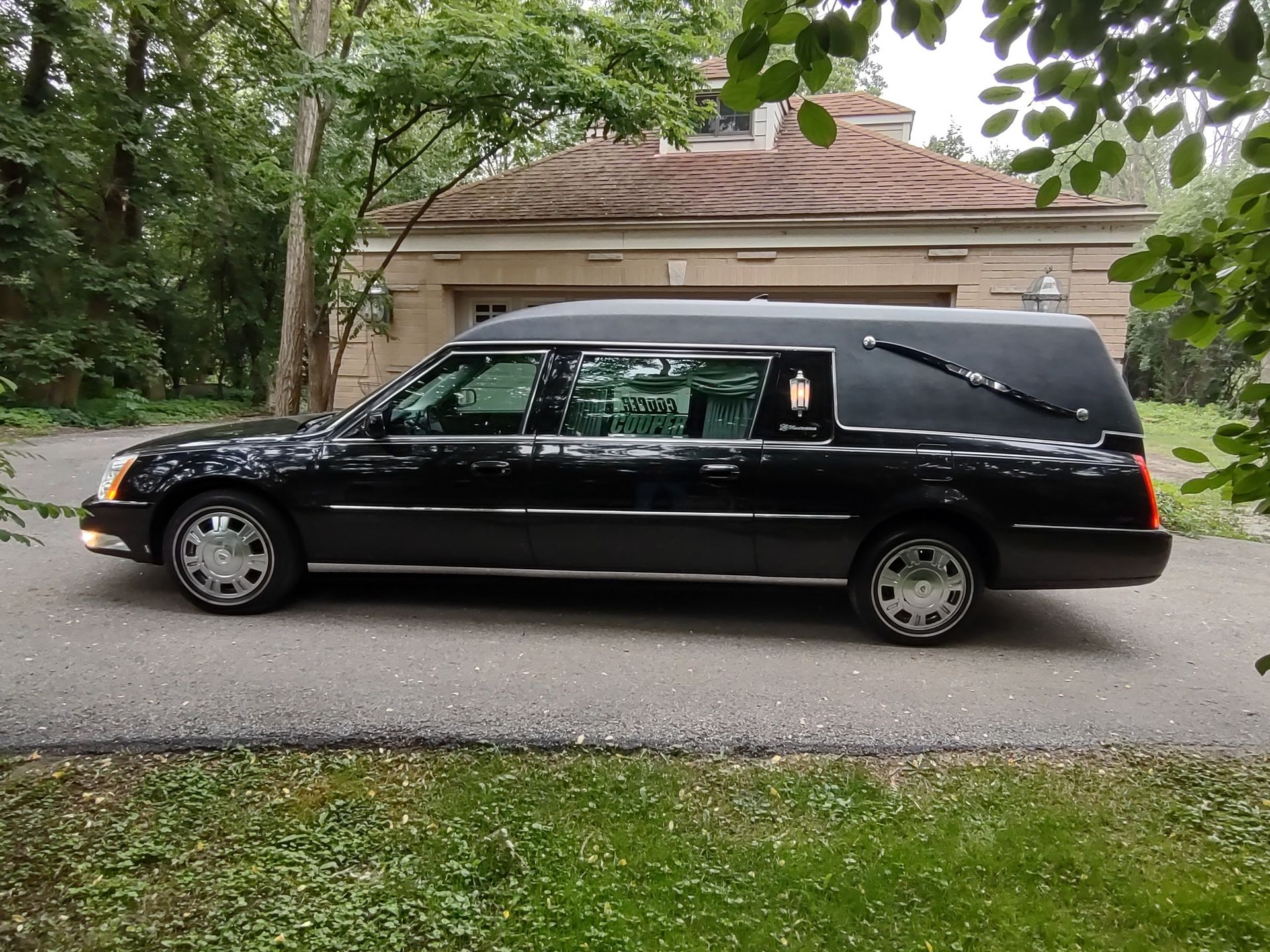 Black hearse parked on a residential street in front of a beige house.