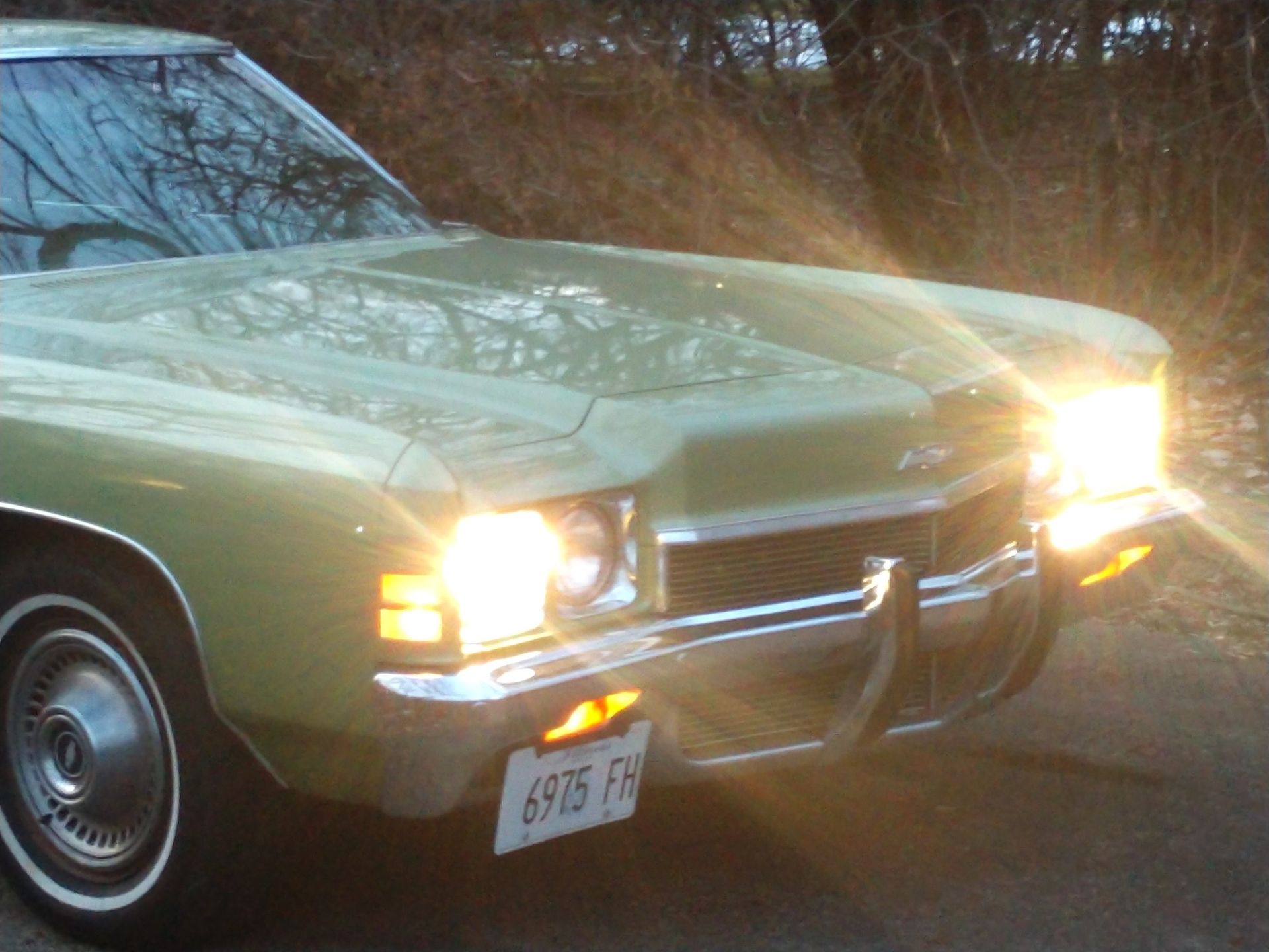 Yellow classic car with headlights on, driving at dusk on a road