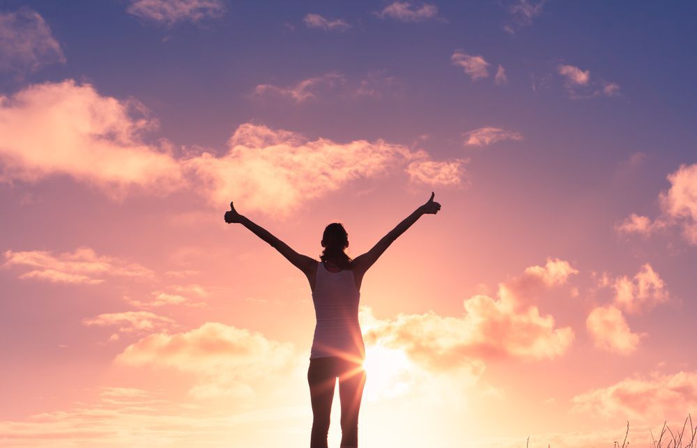 Woman standing infront of a sunset with arms in the air- Adult Therapy on Wurtulla, QLD
