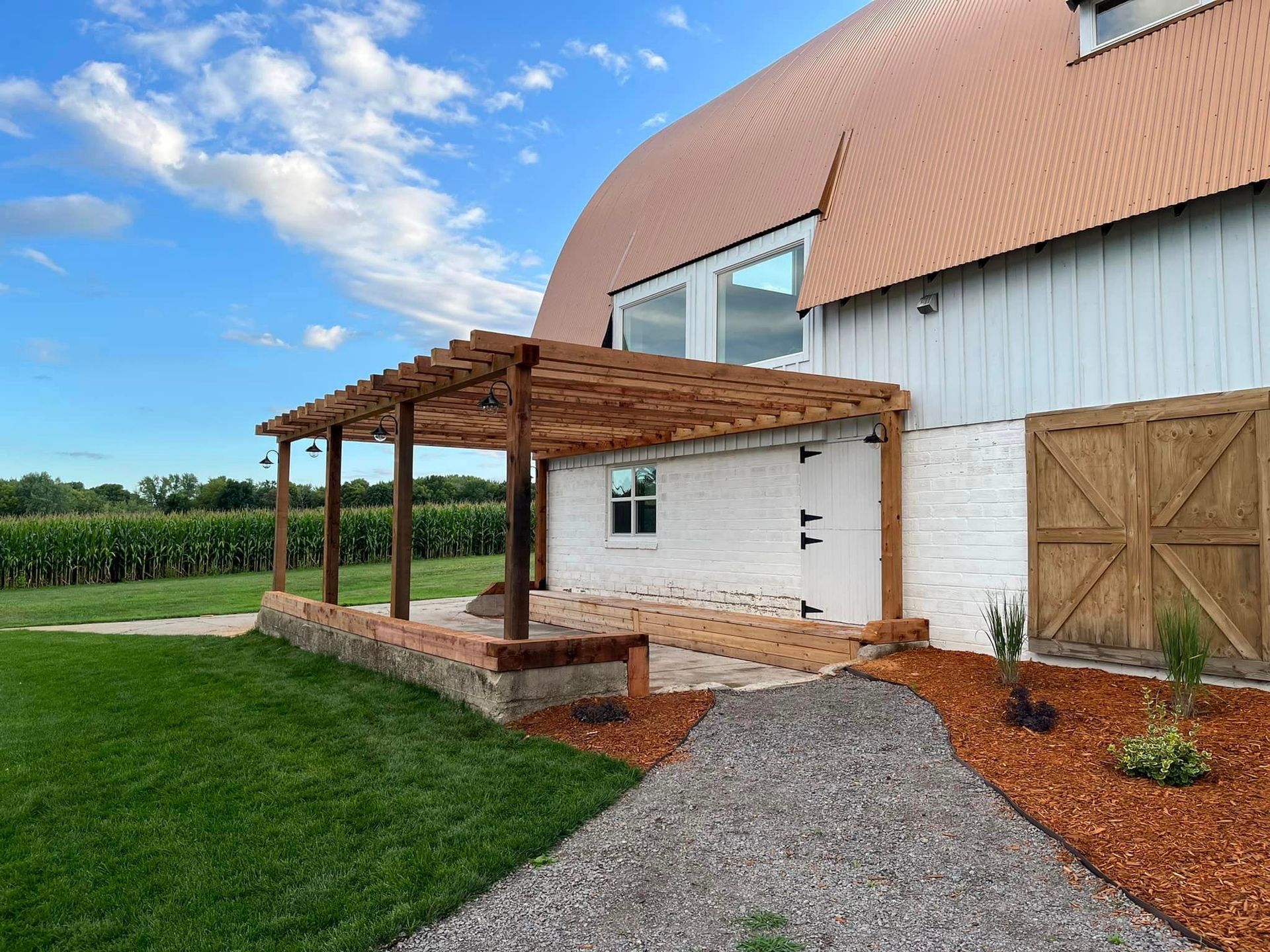 A white barn with a wooden pergola and a walkway leading to it.