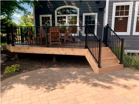A wooden deck with stairs leading up to it is in front of a house.