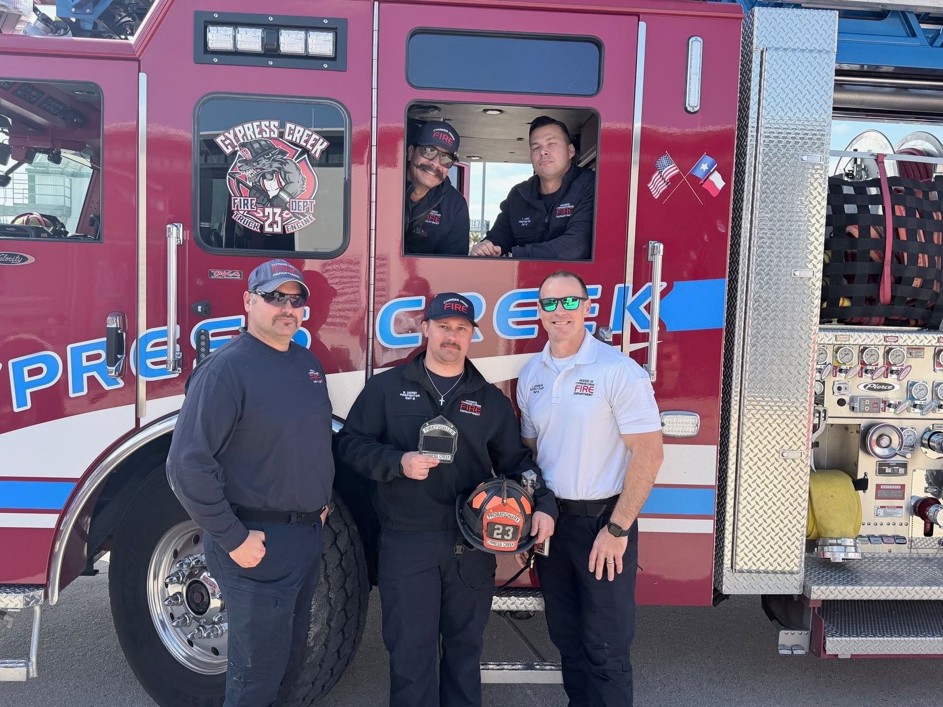 Four people posing beside a red fire truck with open doors, one holding a small dog.