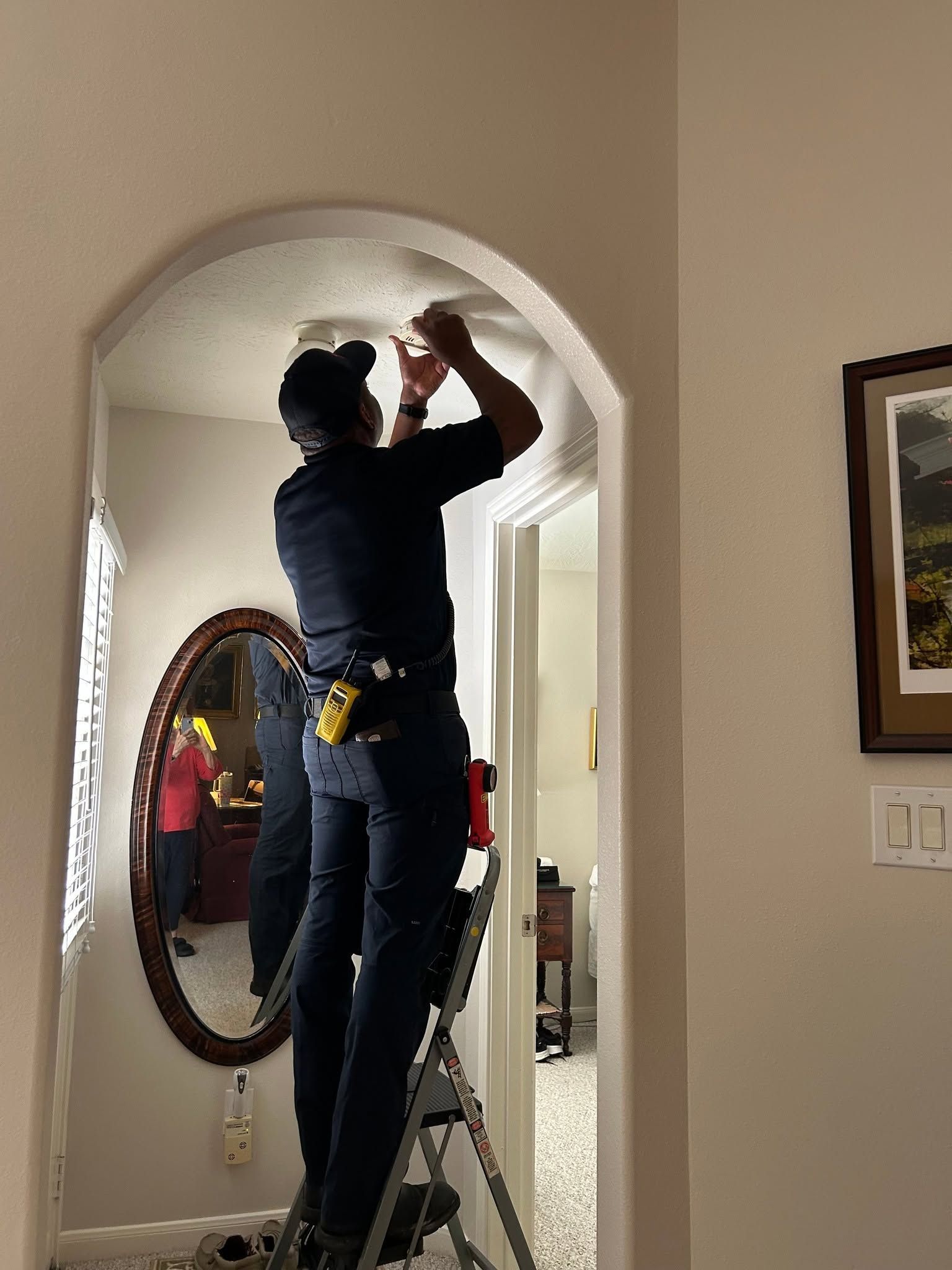 Person on a step ladder painting the top of an arched doorway in a hallway.