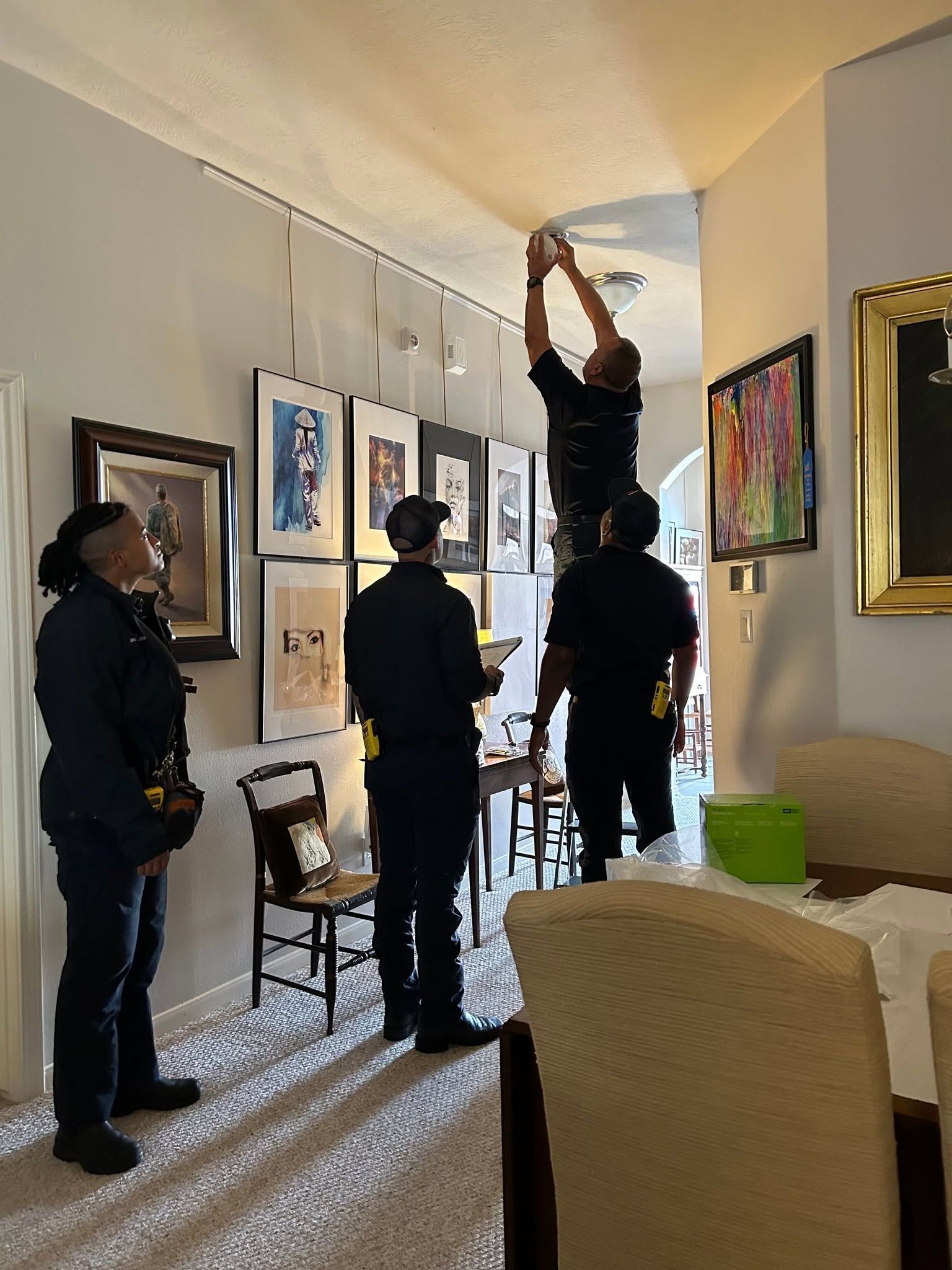 People installing framed art in a narrow hallway, one on a ladder, others standing nearby.