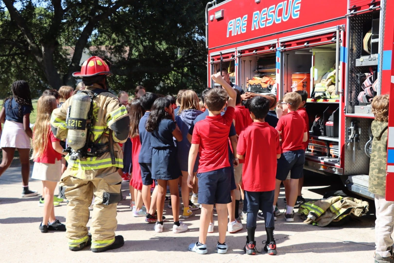 Fire rescue truck parked while a firefighter speaks with children outside a building