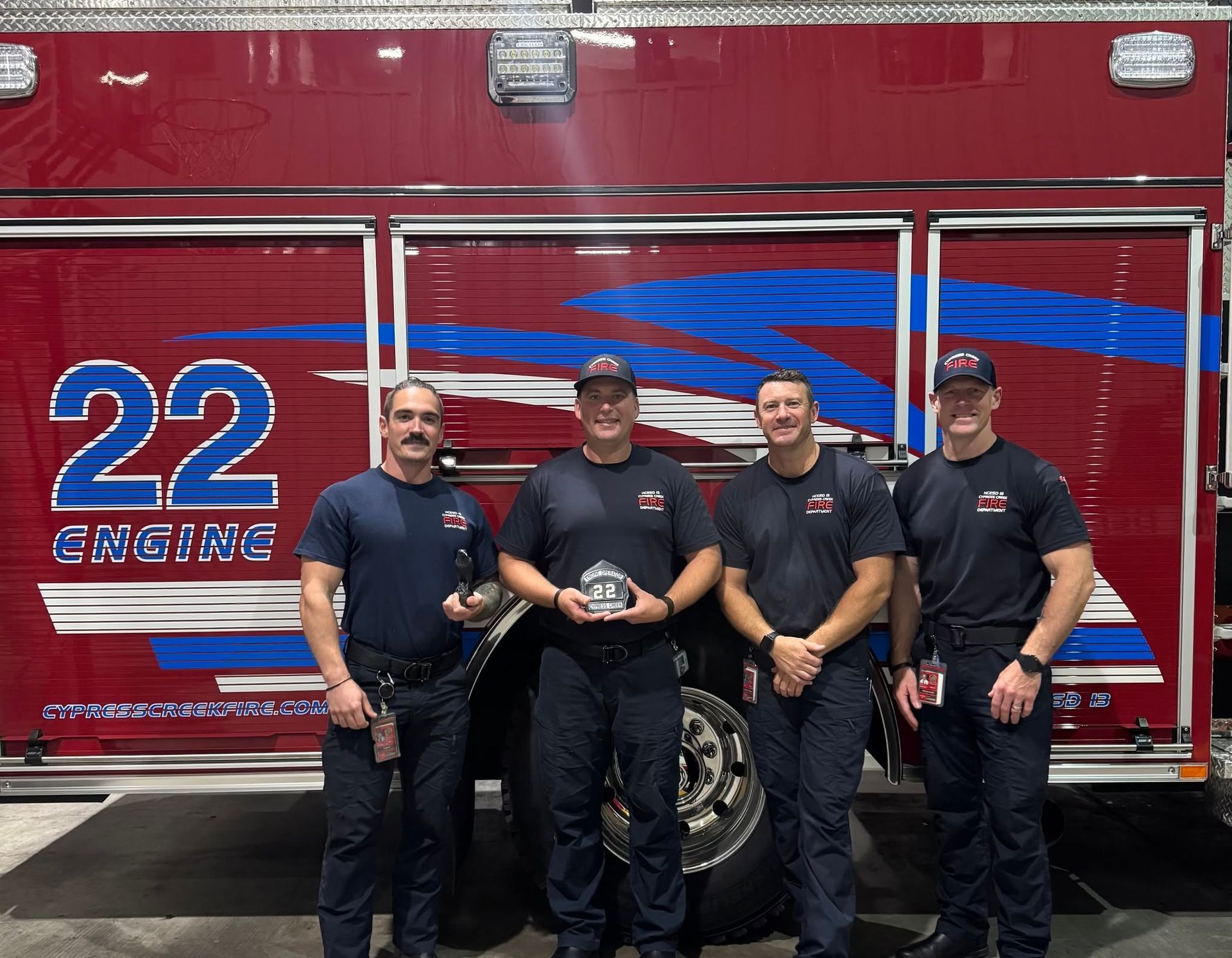 Four firefighters standing in front of a red rescue truck marked 22 EMS.