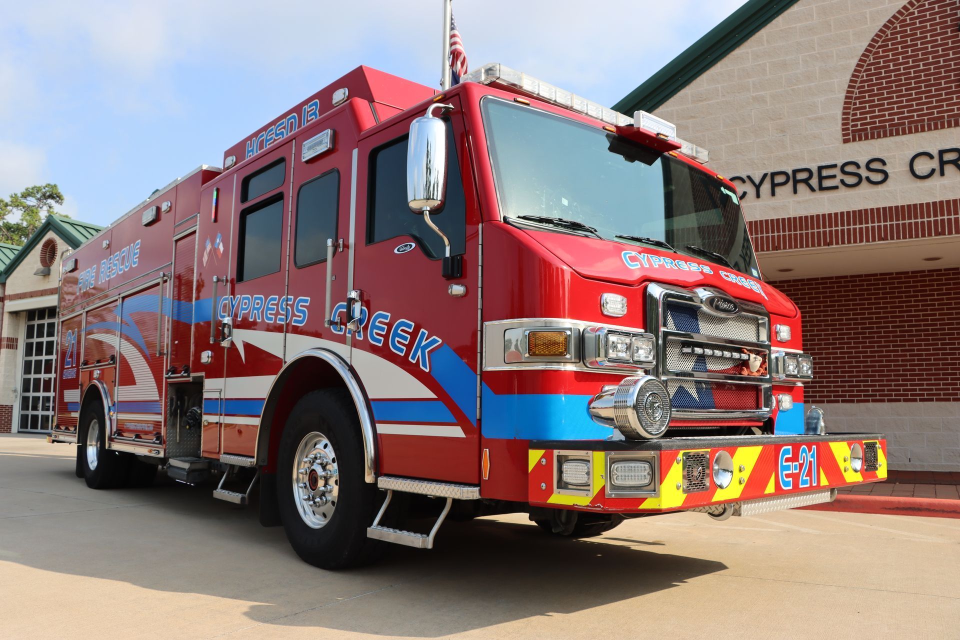 A red and blue fire truck is parked in front of a brick building. Cypress Creek fire engine 21